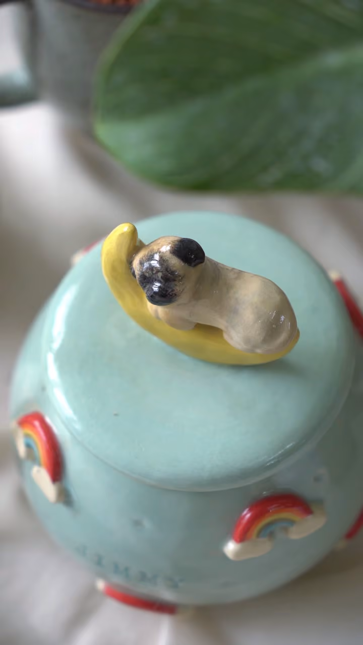 A sequence of finished ceramic urns, each with a different pet’s name and figurine on the lid