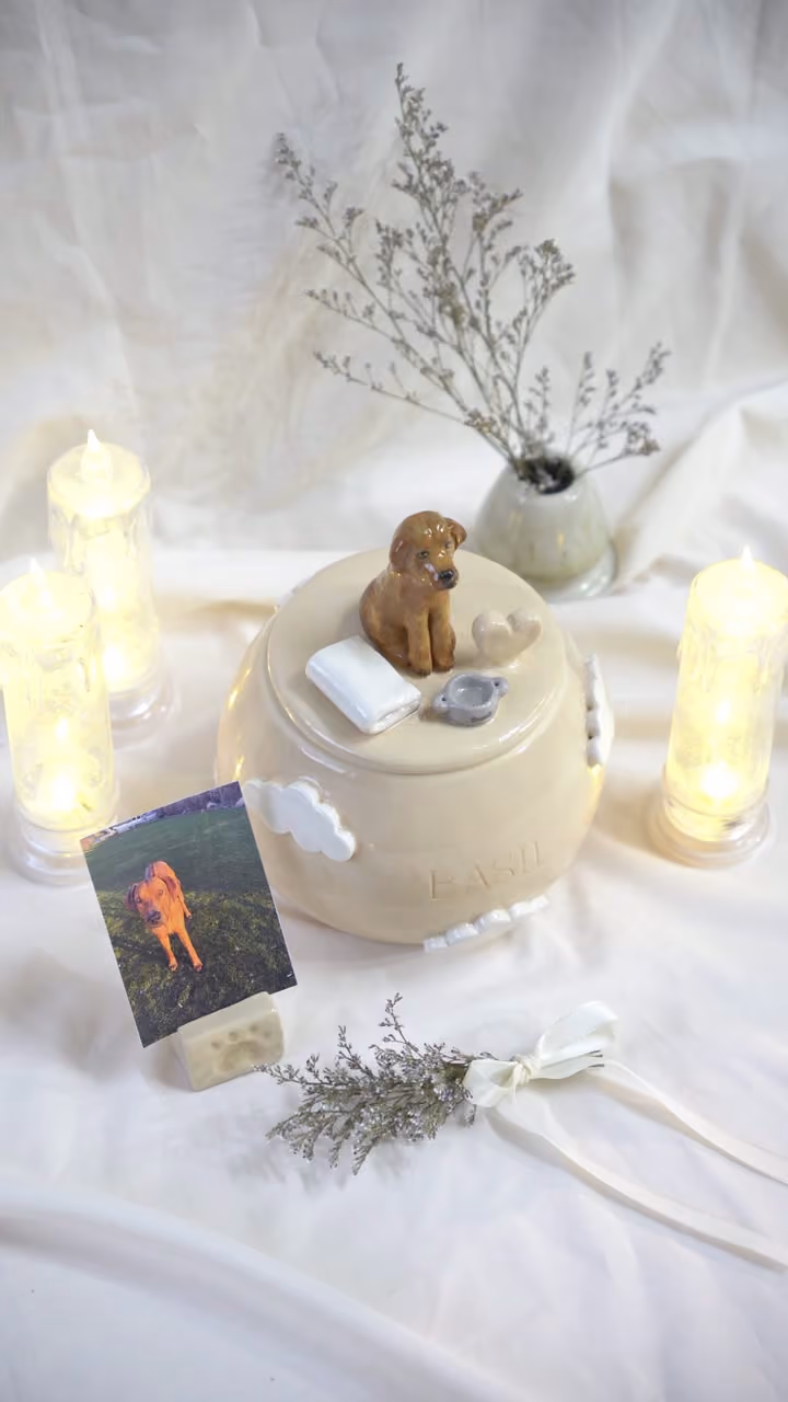A finished ceramic urn with Basil’s name on it, filmed beside a photo of Basil
