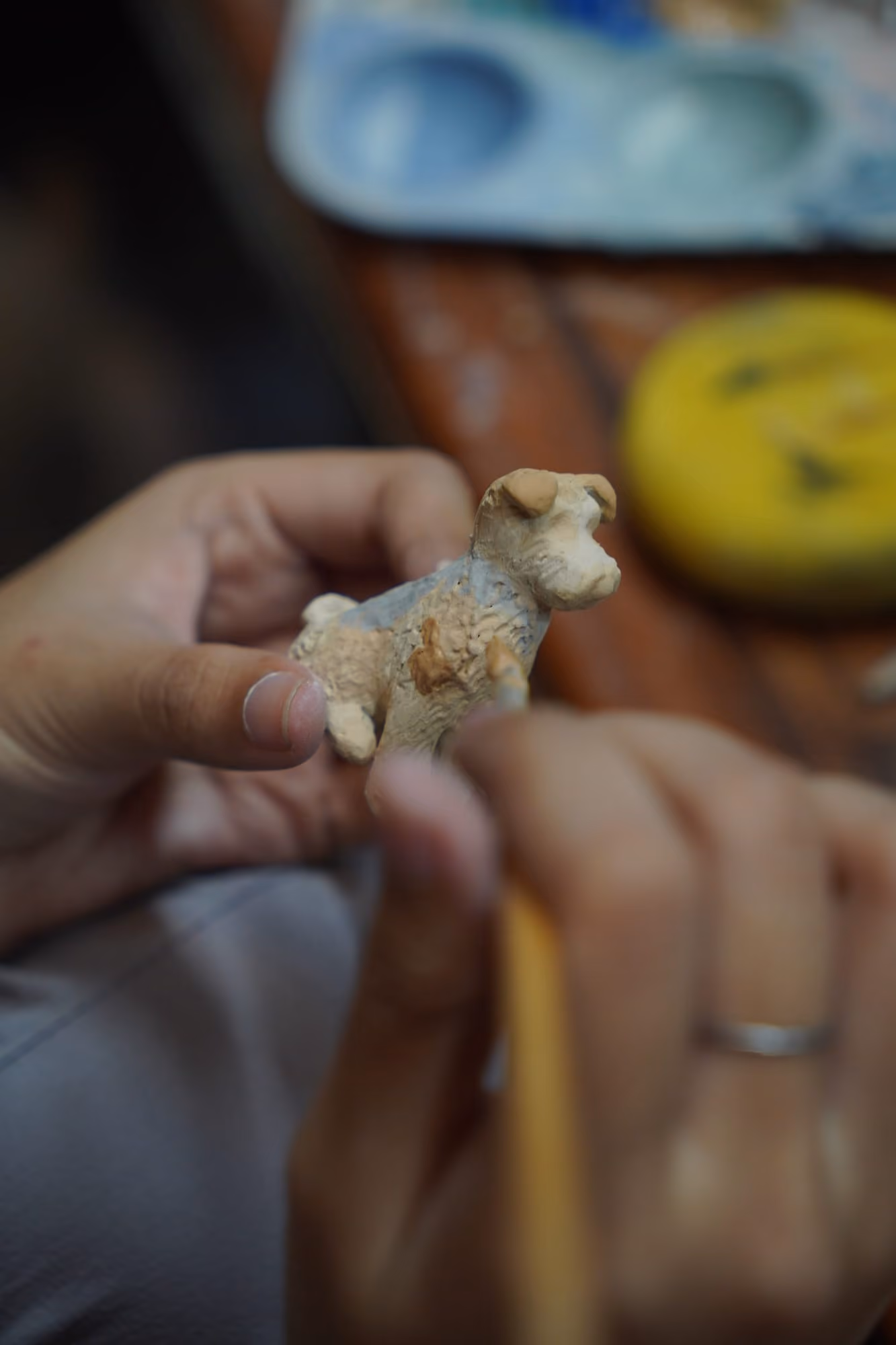 Fingers holding a tiny clay dog figurine while a thin tool adds detail to its face