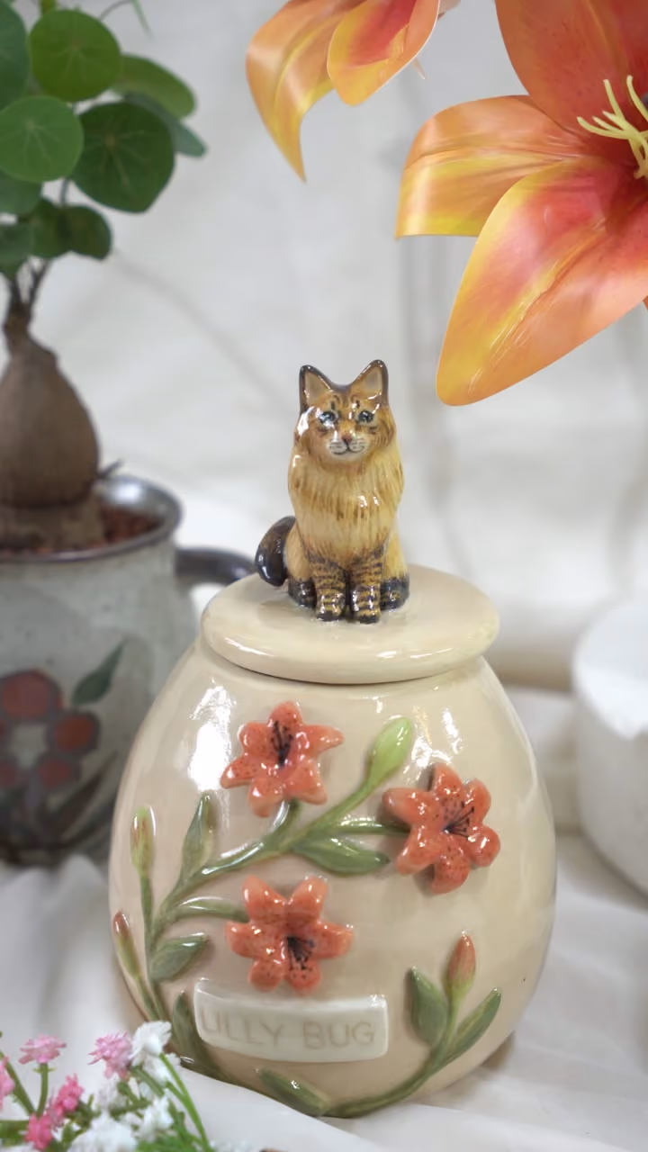 A finished ceramic urn with Lily Bug’s name on it, filmed beside a photo of Lily Bug