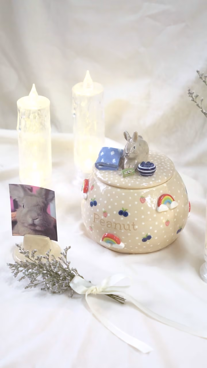 A finished ceramic urn with Peanut’s name on it, filmed beside a photo of Peanut