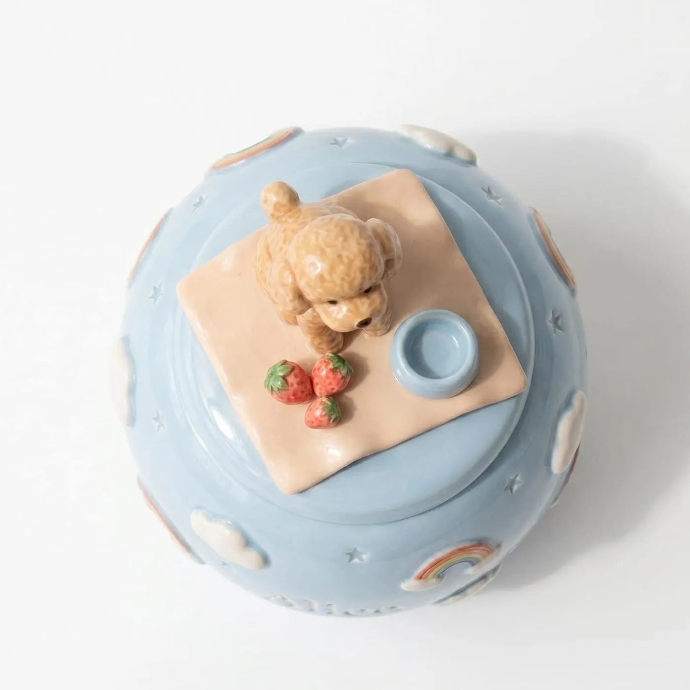 The same jar seen from directly above, showing the poodle sitting on a peach blanket that covers most of the lid, with three strawberries in front and a small blue bowl to one side