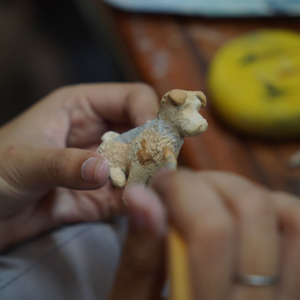 Artisan hand-sculpting a small clay dog figurine with a wooden modelling tool